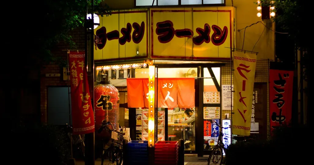 夜晚灯火通明的小餐馆门面，门口挂着招牌和旗帜