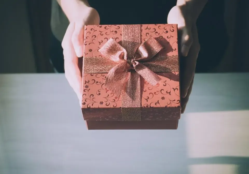 Dua tangan memegang kotak hadiah merah muda berpita