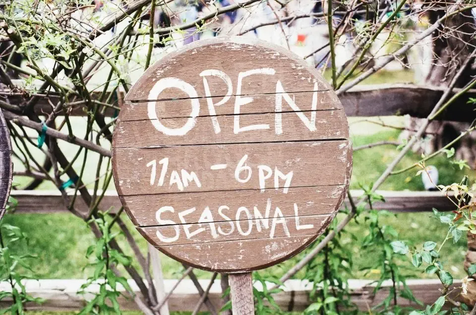 ป้ายไม้ทรงกลมเขียนว่า OPEN 11AM – 6PM แขวนหน้าร้าน