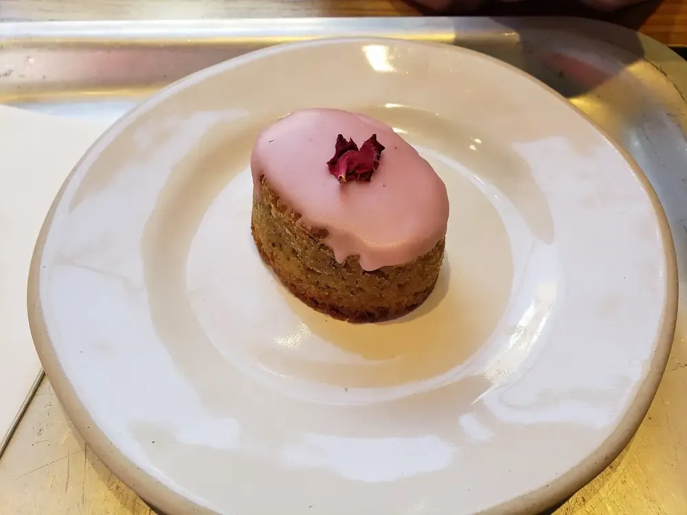 Kue kecil berlapis icing merah muda dihias kelopak mawar, di atas piring putih